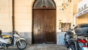 A closed dark wooden door with a decorative metal arch above it, a scooter parked to the left, and a motorcycle to the right. - GuestHost - Modern Two-Levels Apartment with Balconies! (Palermo)