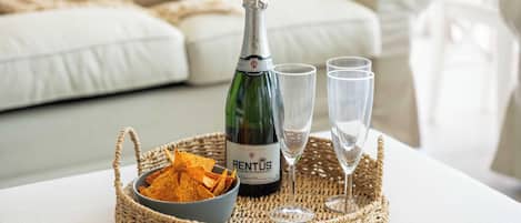 En flaska champagne, två glas och en skål med chips på ett flätat bricka.