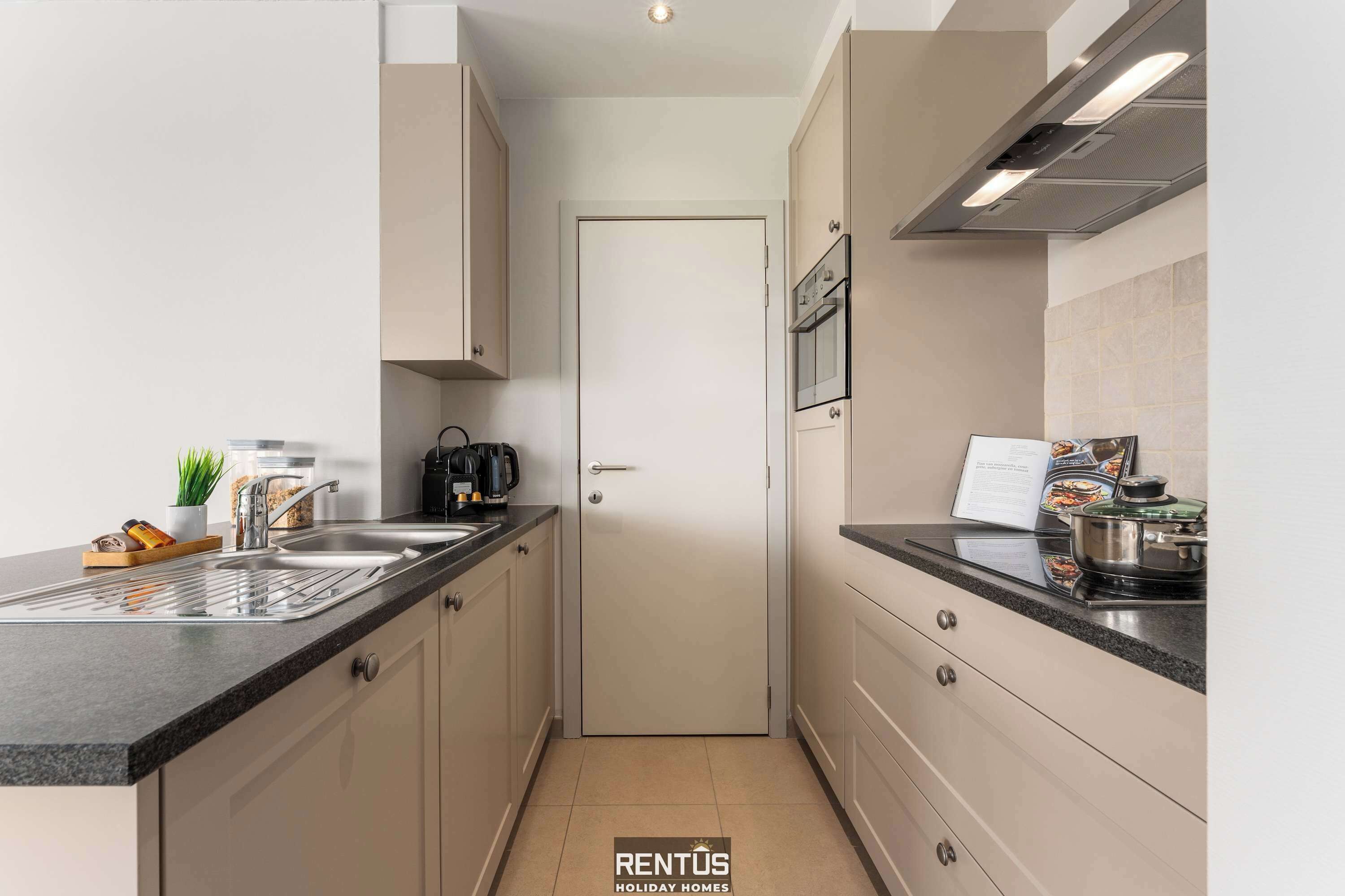 Une cuisine moderne avec un plan de travail noir, des appareils en acier inoxydable et des meubles de couleur beige.