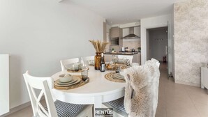 A modern dining area with a round table set for four, white chairs, and a kitchen in the background. - Seange - with beautiful view and many facilities (Nieuwpoort)