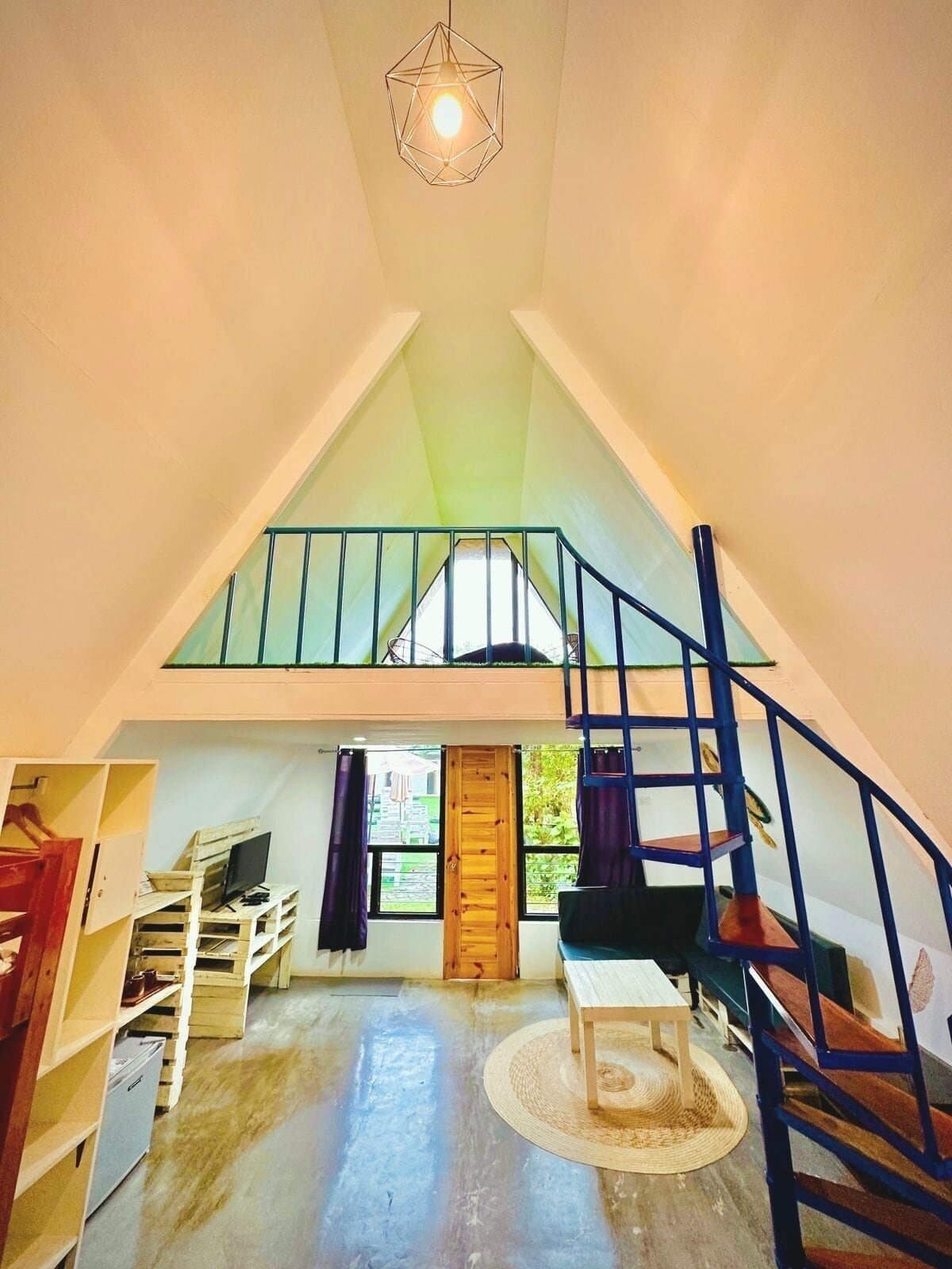 Un espacio tipo loft con techo inclinado, una escalera, una puerta de madera y una pequeña mesa redonda.