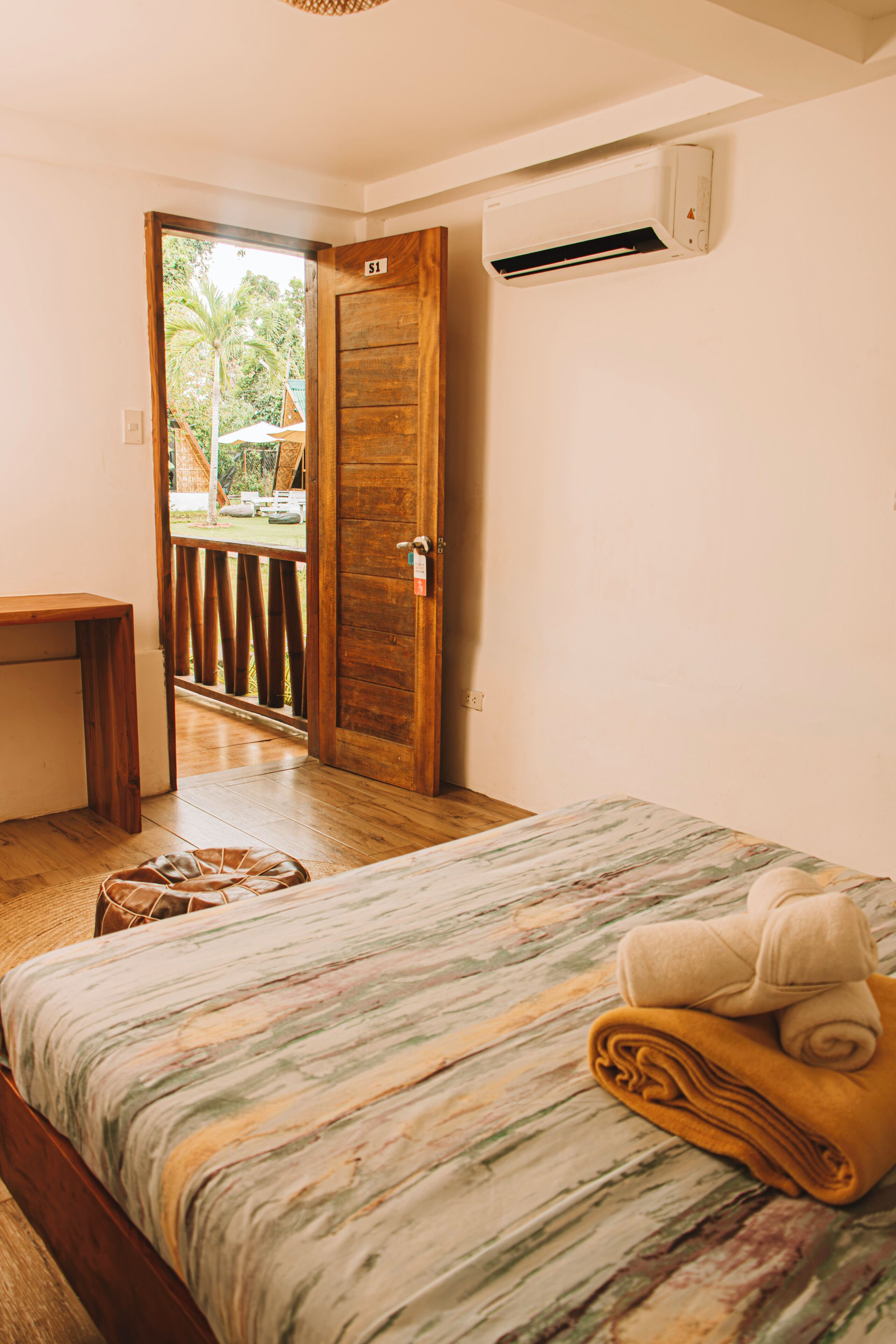 A bedroom with a bed, a wooden desk, and a door leading to an outdoor area.