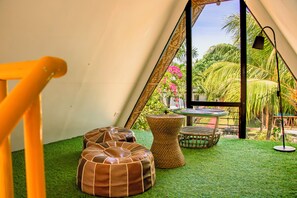 Un interior acogedor con piso de césped artificial verde, un reposapiés de mimbre, una mesita redonda y una silla.