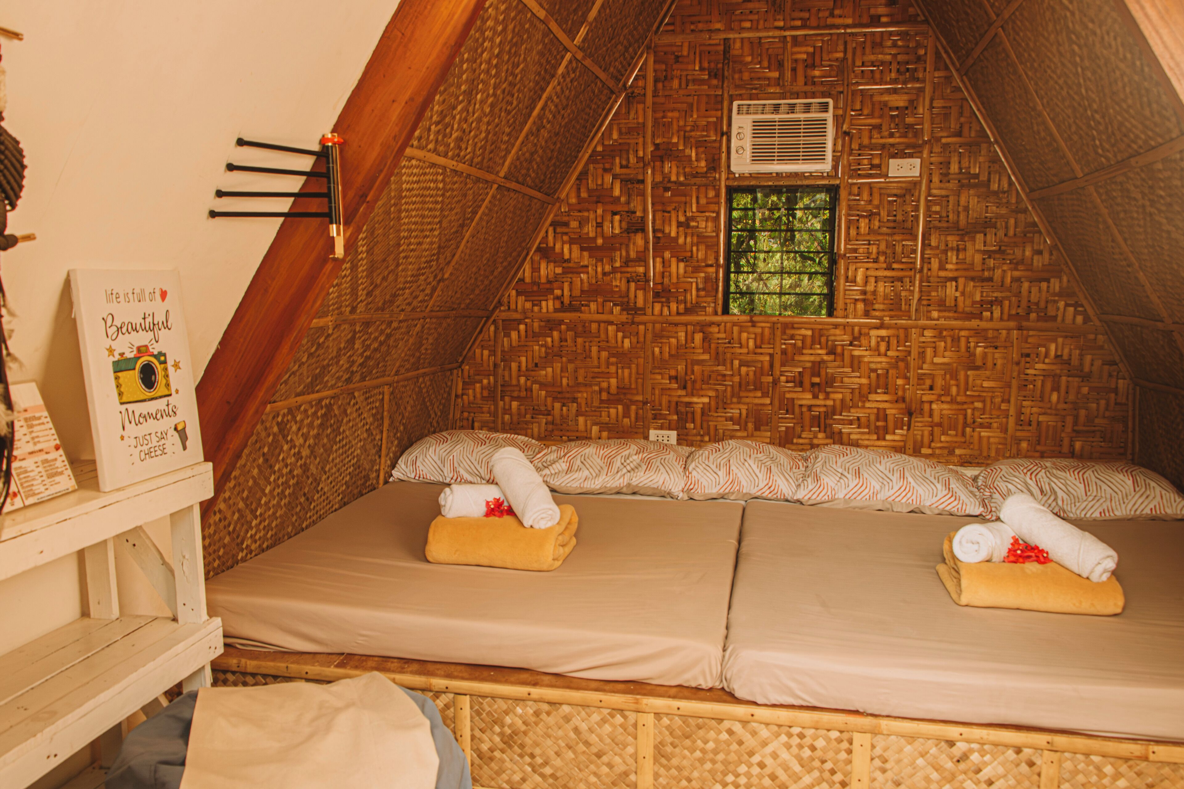 A cozy, triangular room with a woven ceiling, a bed with two pillows, and a small window.