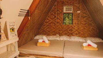 A cozy, triangular room with a woven ceiling, a bed with two pillows, and a small window.