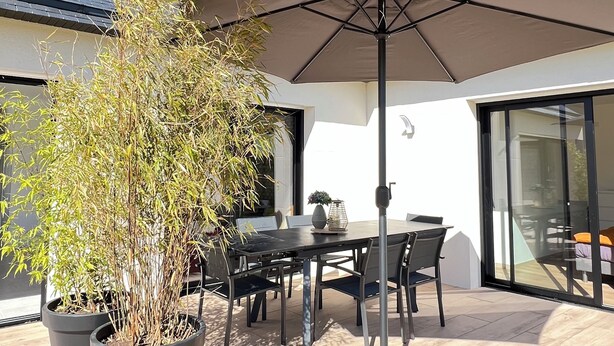 Eine Terrasse mit Tisch, Stühlen, einem großen Sonnenschirm und Blumentöpfen.