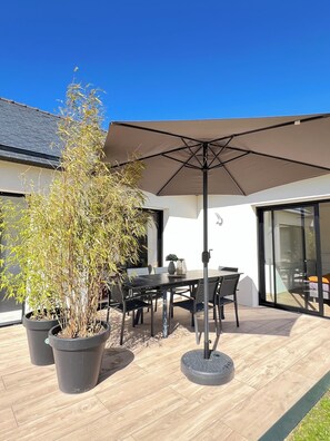 Une terrasse avec une table et des chaises, un grand parasol et des plantes en pot.