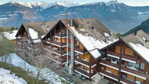 Un chalet en bois à plusieurs étages, doté de balcons, qui se dresse sur fond de montagnes enneigées.