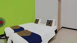 Ein Zimmer mit zwei Betten, einer grünen Wand, einer weißen Wand, einem kleinen Fenster und einem Ventilator.