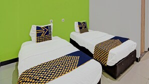 Zwei Einzelbetten mit weißer Bettwäsche und einem Kissenüberwurf in Blau und Gelb, an einer grünen Wand.