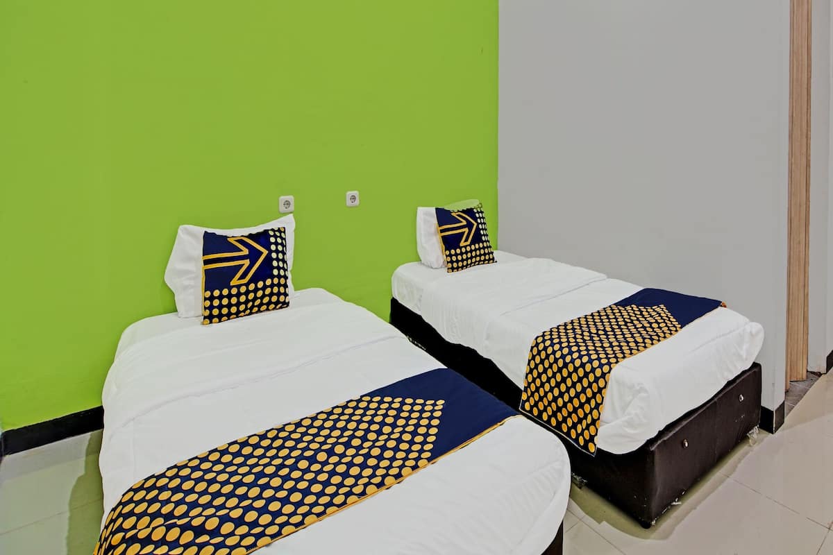 Duas camas de solteiro com roupa de cama branca e edredons estampados em azul e amarelo, diante de uma parede verde.