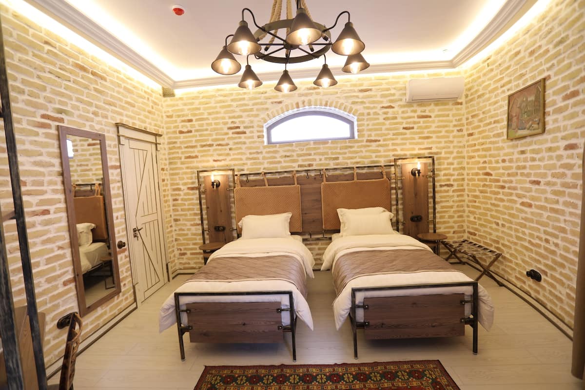 A room with two beds, a chandelier, a window, and a brick wall.