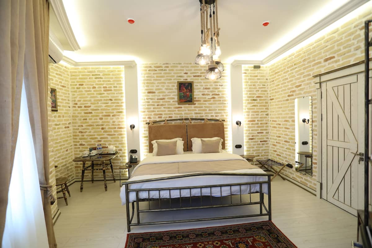 A bedroom with a brick wall, a bed with a headboard, a small table, and a chair.