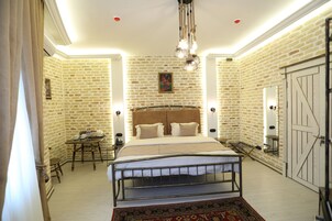 Quarto com parede de tijolos, uma cama com cabeceira, uma mesinha e uma cadeira.