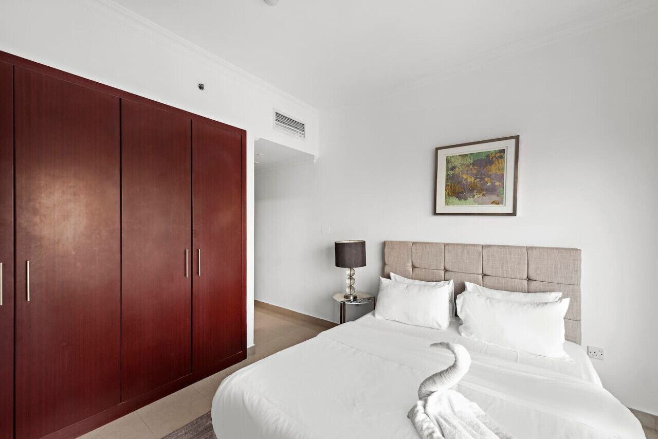 Habitación de hotel con una cama grande, un armario, una mesita de noche con lámpara y un cuadro en la pared.