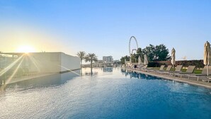 Ein Swimmingpool mit Sonnenstrahlen, Liegestühlen und einem Riesenrad im Hintergrund.