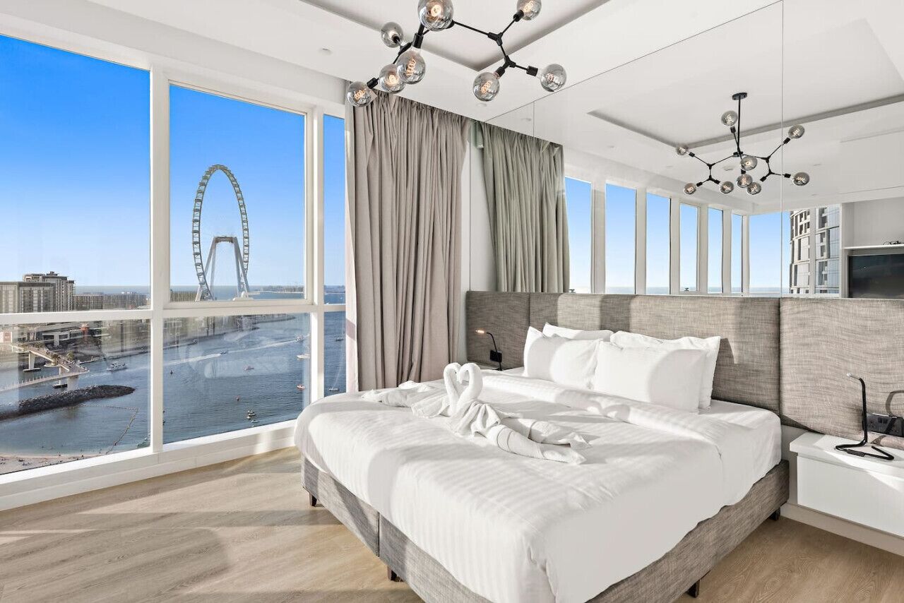 A modern hotel room with a large bed, a view of a Ferris wheel, and a cityscape.
