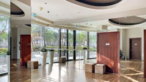 A modern lobby with wooden flooring, large windows, and a glass partition.
