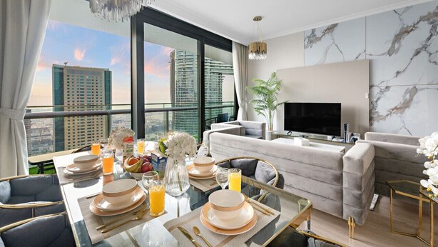 A modern hotel room with a dining area, a living space, and a large window offering a city view.