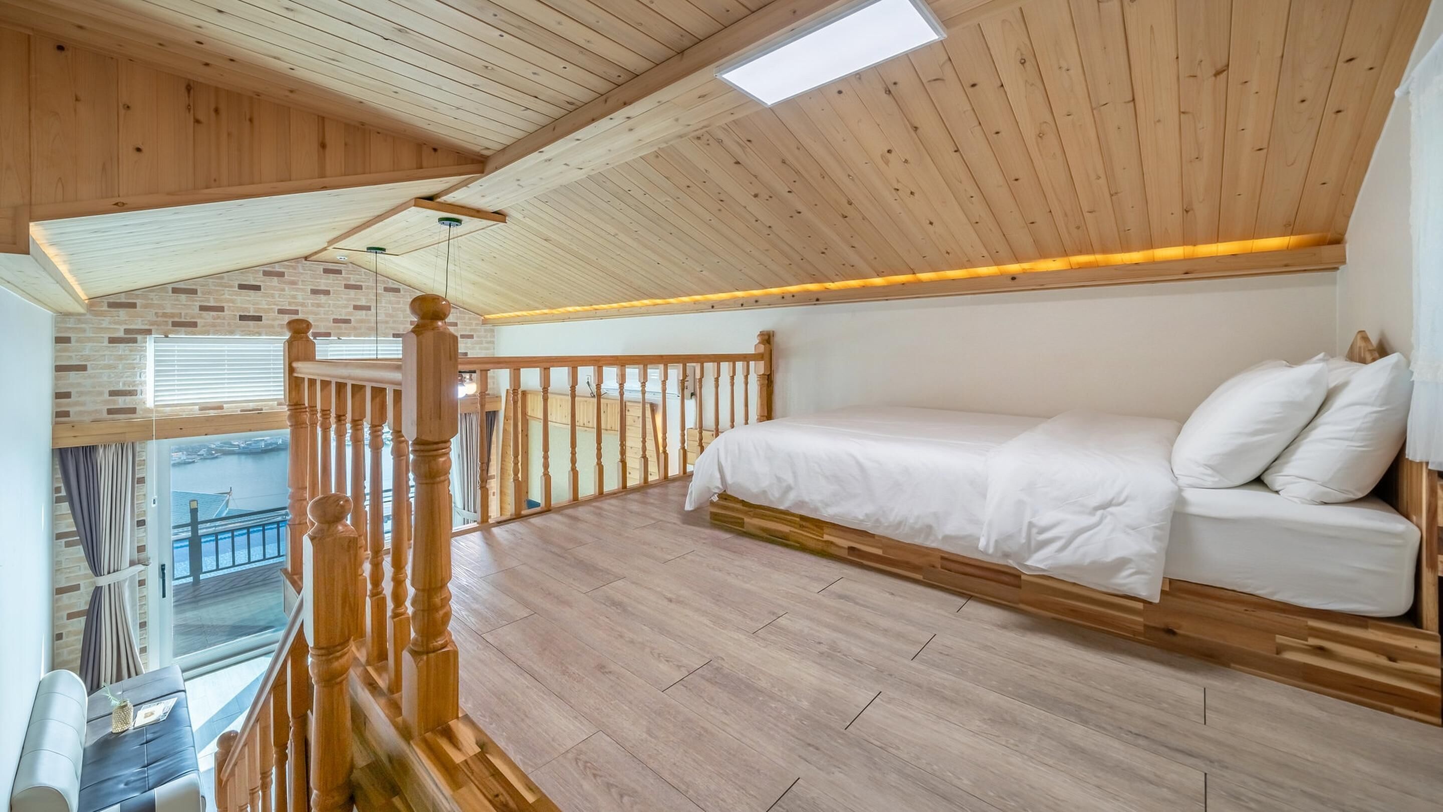 A loft bedroom with a wooden ceiling, a bed, a balcony, and a view of a boat.
