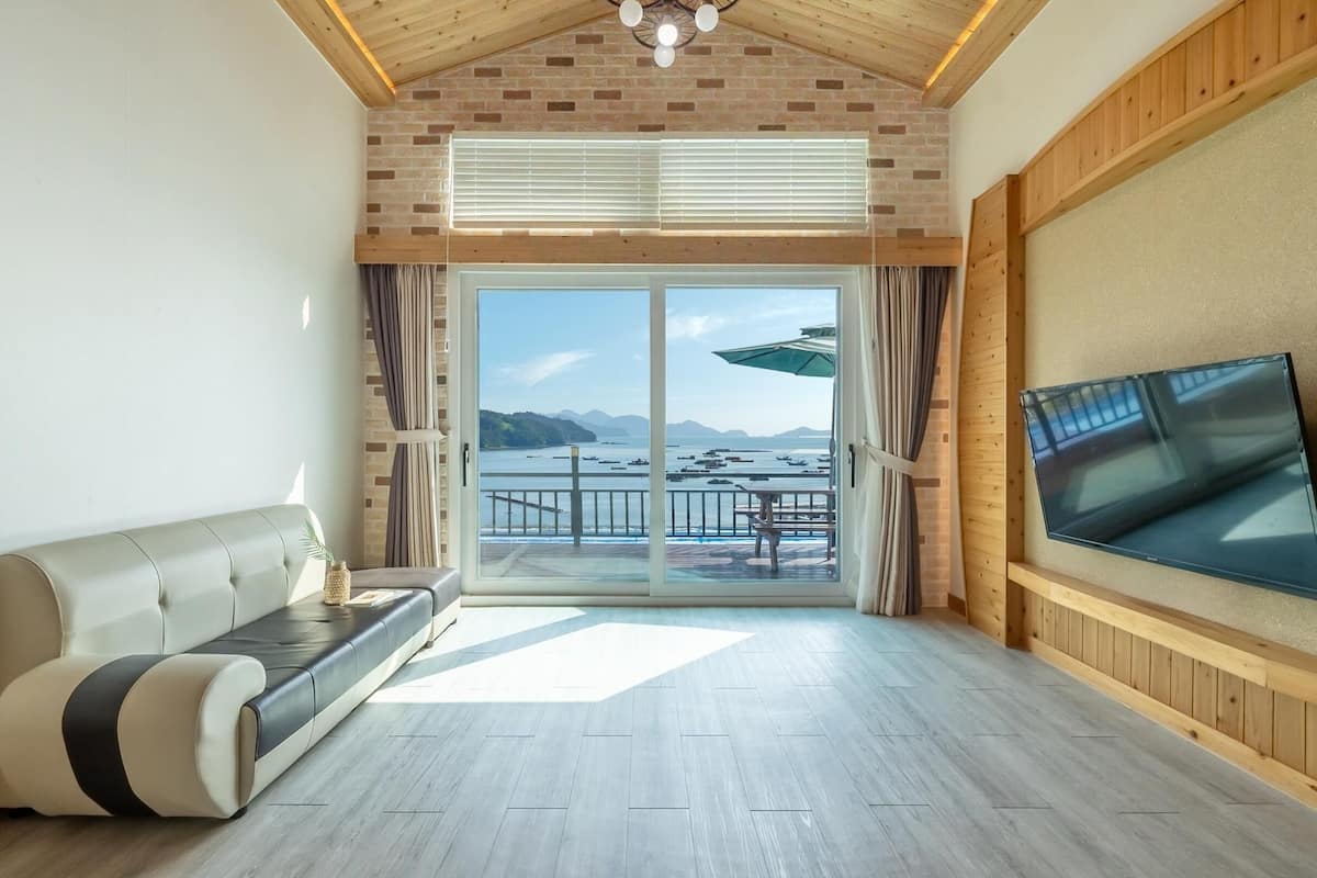A modern living room with a sofa, a TV, and a view of the sea.