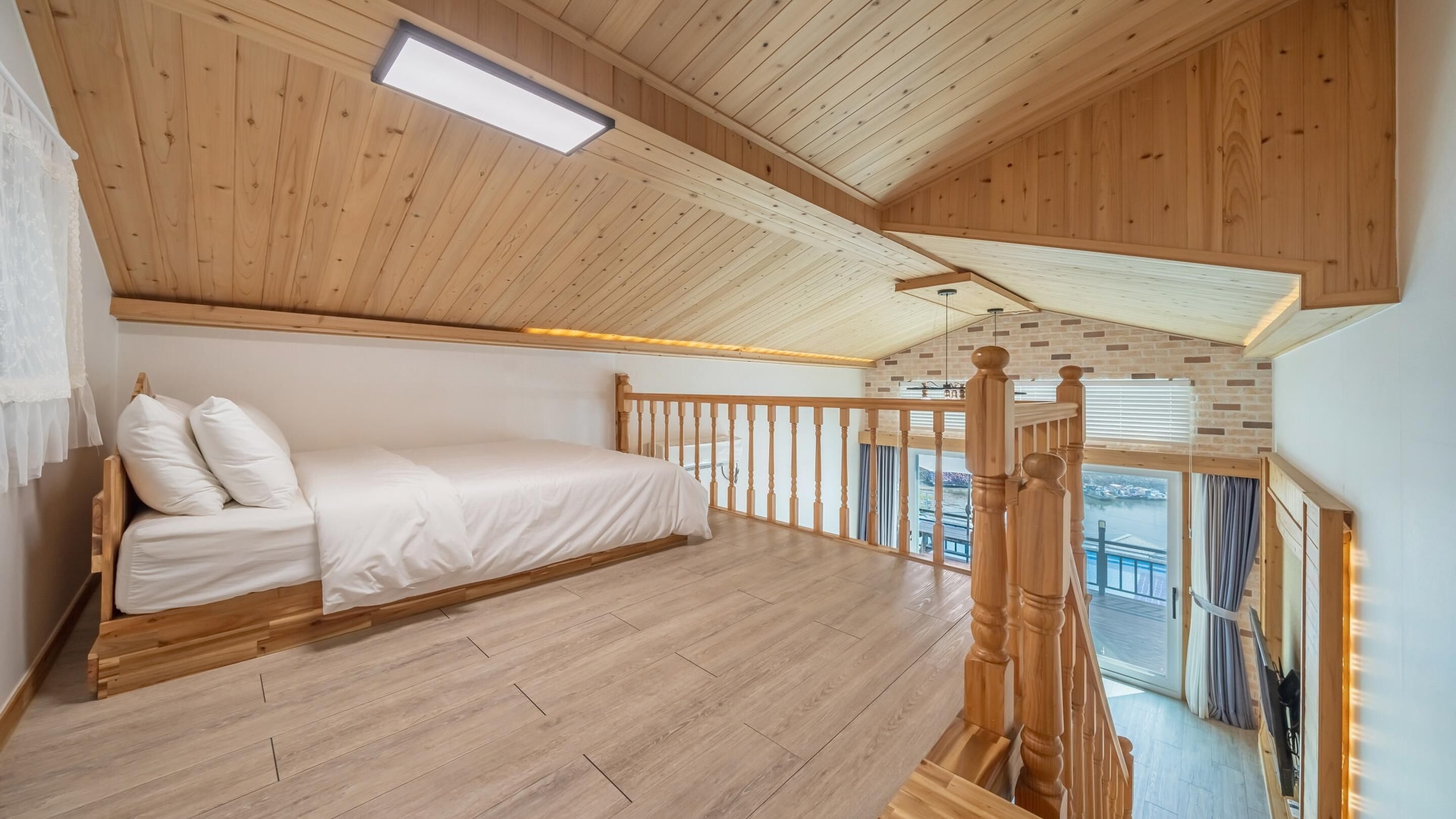 A bedroom with a wooden bed, a wooden floor, a balcony with a wooden railing, and a view of the outside.