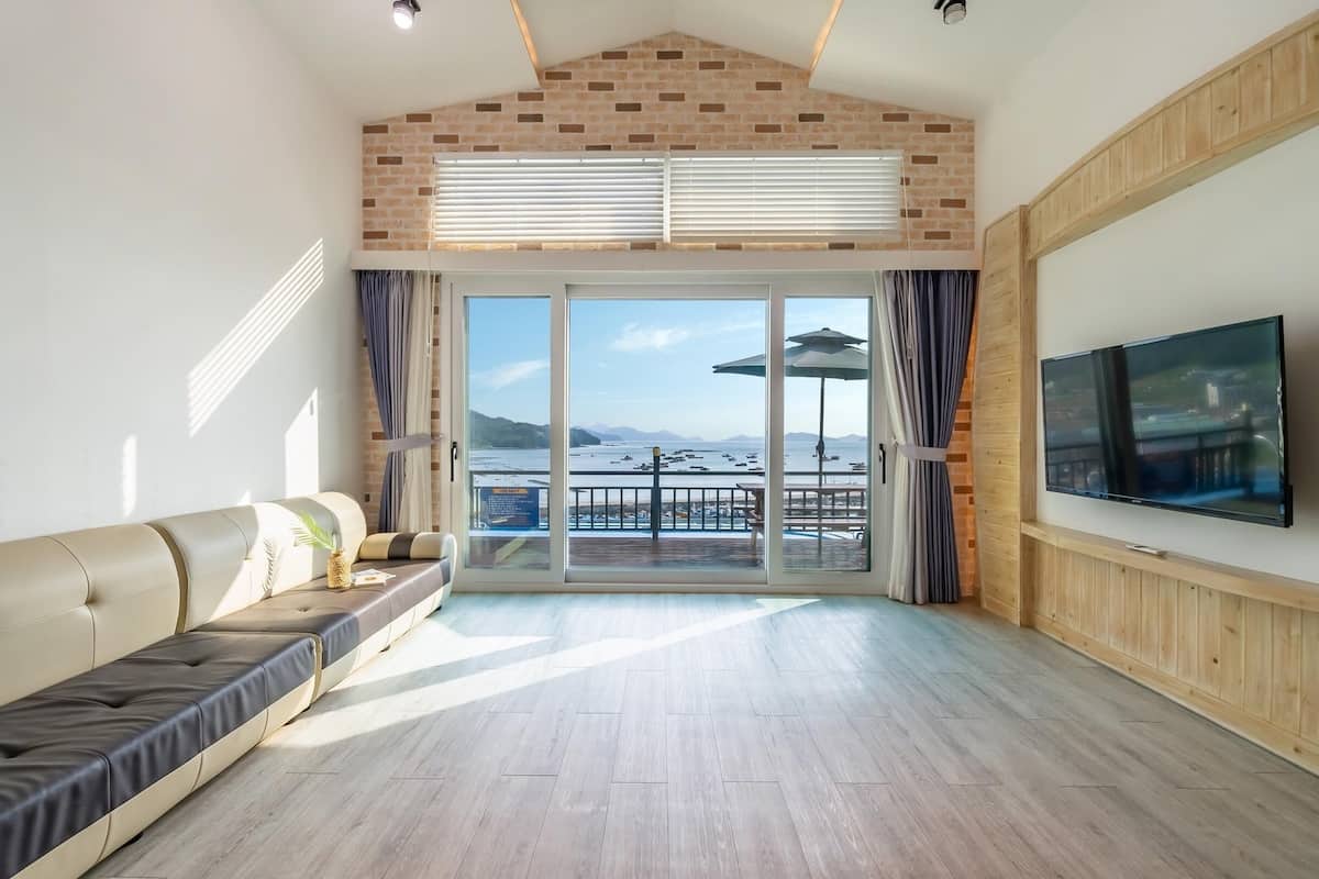 A spacious living room with a large sliding glass door leading to a balcony with a view of the sea.