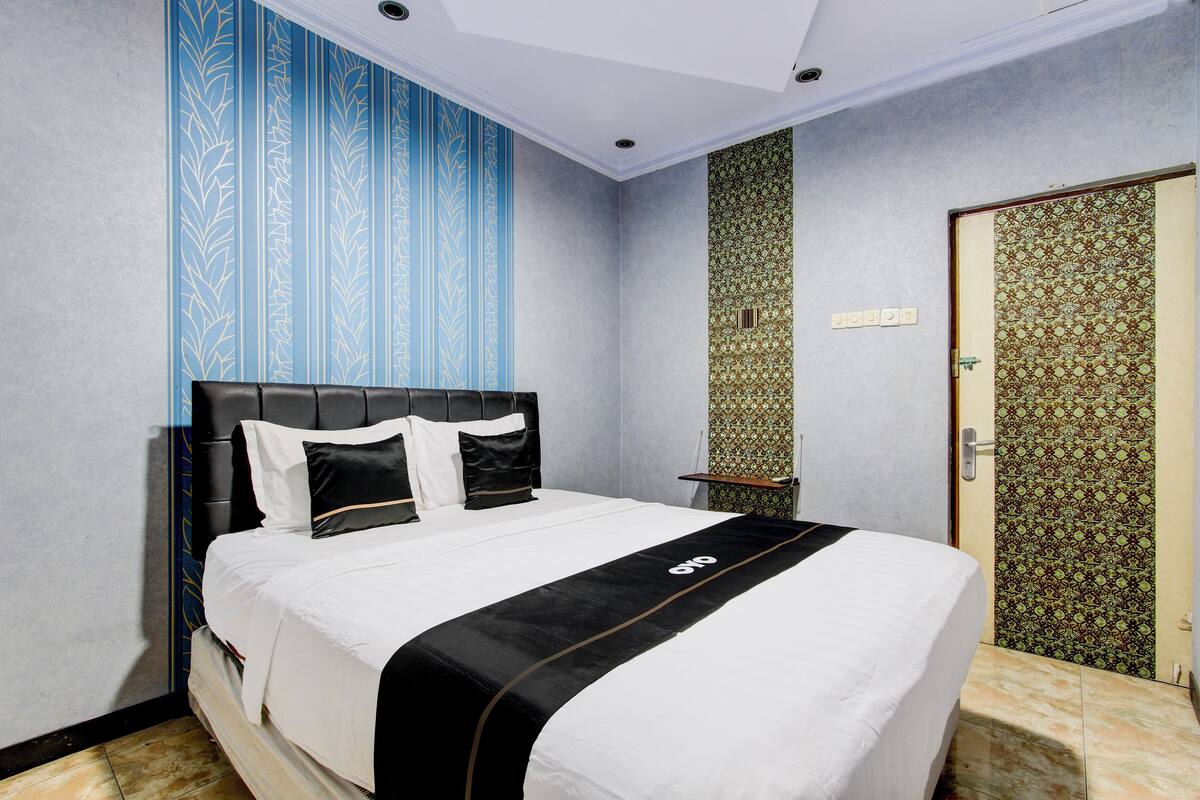 Una cama bien hecha con colcha blanco y negro, cabecera y pared con papel tapiz de rayas verticales azules y verdes.