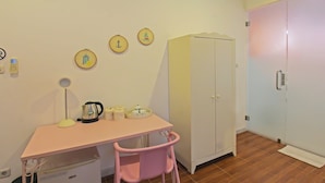 Une petite pièce avec un bureau rose, une armoire blanche et une chaise rose. Il y a quatre éléments de décoration au mur et une petite poubelle.