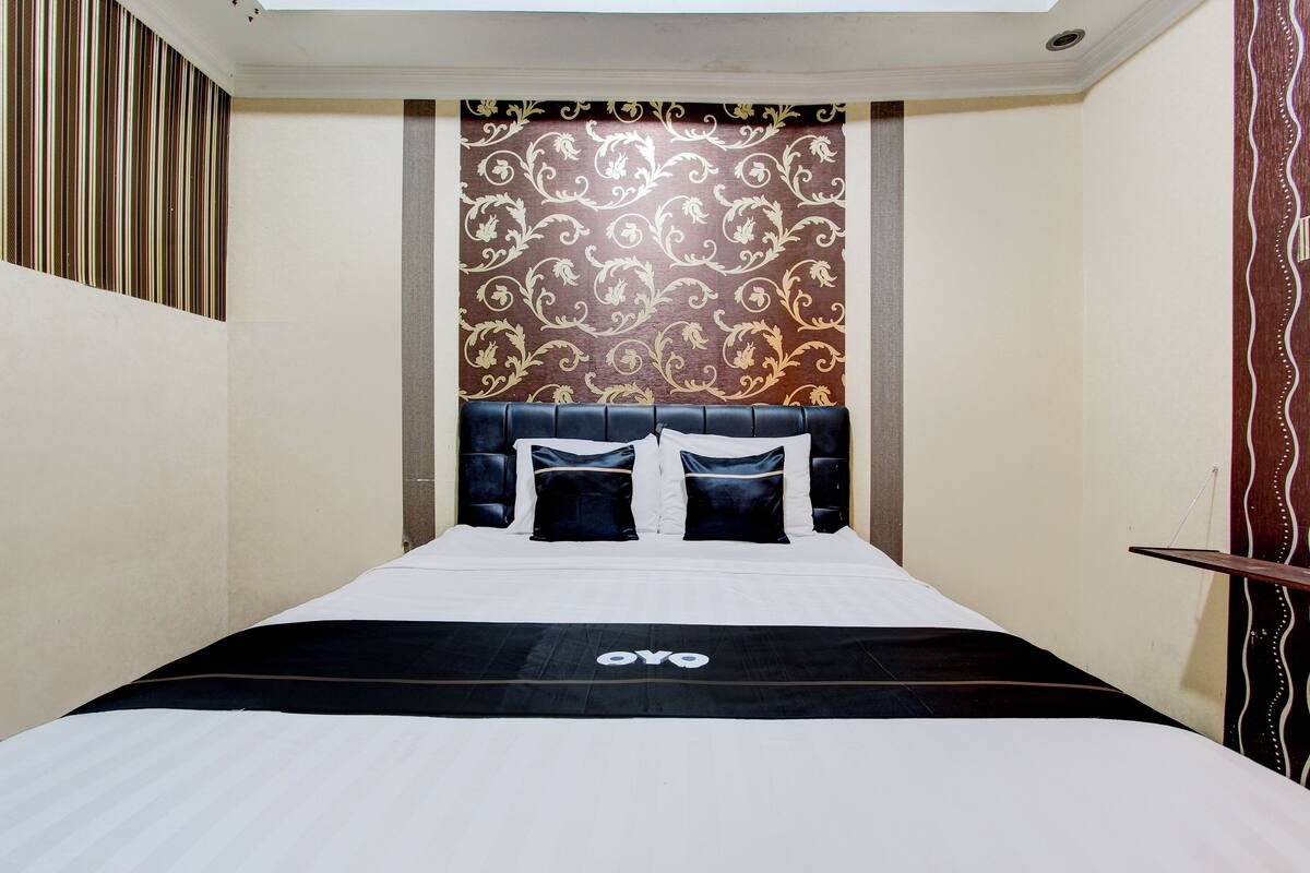 Una habitación de hotel con cama, cabecera y pared estampada.