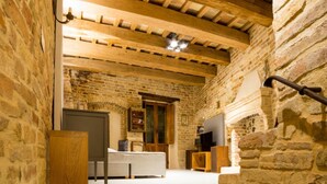 A rustic room with exposed brick walls, a wooden ceiling, a bed, a television, and a small table. - The Monastery - Unique Vacation Home (Monteprandone)