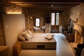 A cozy room with a bed, a wooden bench, a fireplace, and a stone wall.