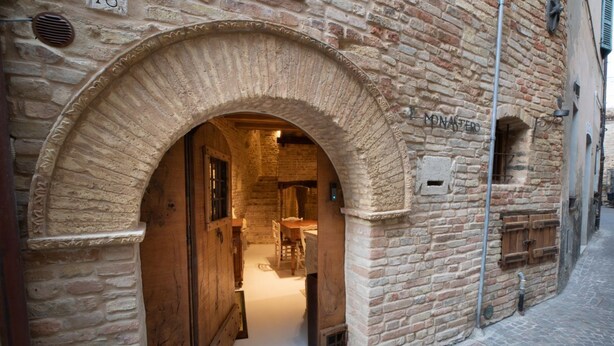 An arched doorway leading into a room with a wooden table and chairs, a brick wall, and a sign reading 'MONASTERO'. - The Monastery - Unique Vacation Home (Monteprandone)