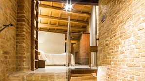 A narrow stone corridor leading to a room with a bed, wooden beams, and a brick wall. - The Monastery - Unique Vacation Home (Monteprandone)