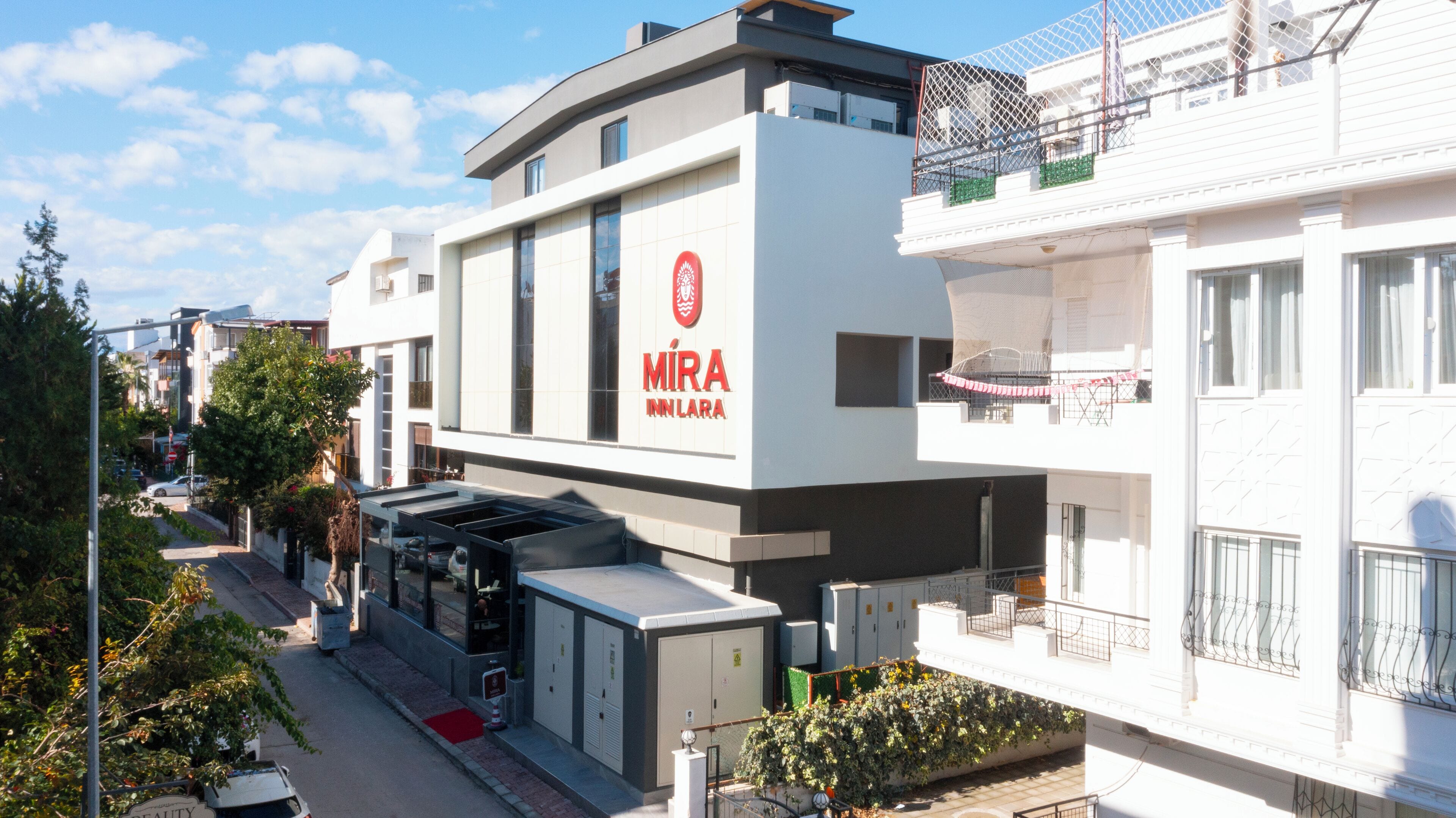 Un hotel moderno con un llamativo letrero 'MIRA INN LARA', que presenta un diseño limpio y contemporáneo con techo plano y grandes ventanales.