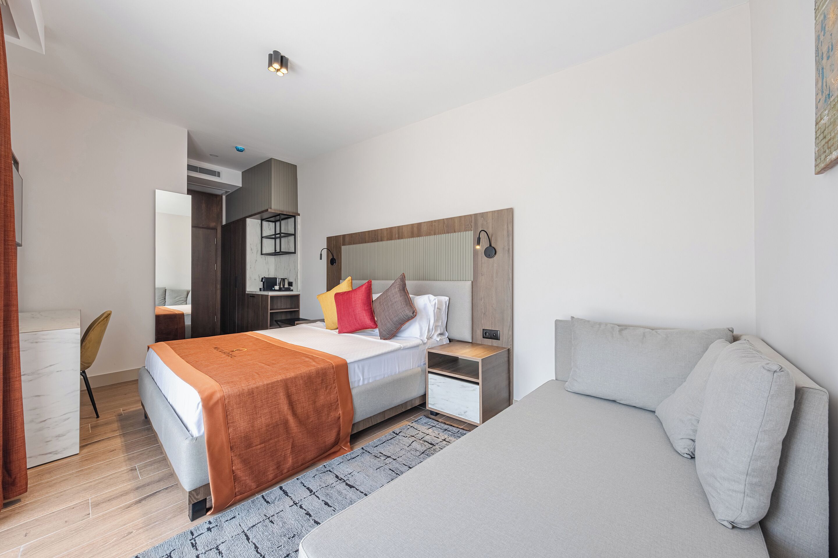 Una habitación de hotel moderna con una cama, un sofá, un escritorio y un espejo.