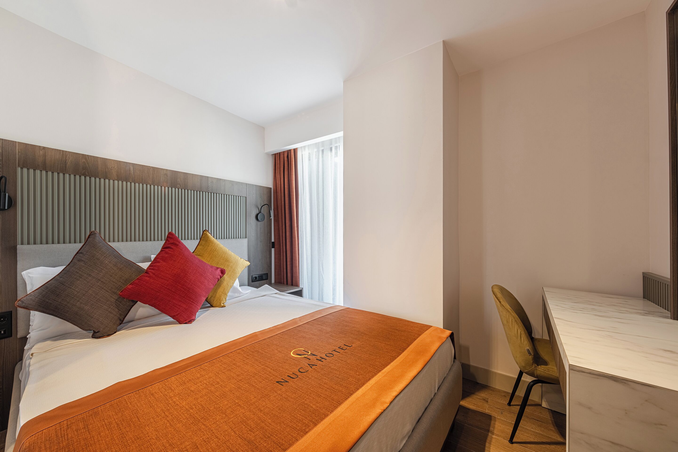A hotel room with a bed, a desk, and a window with curtains.