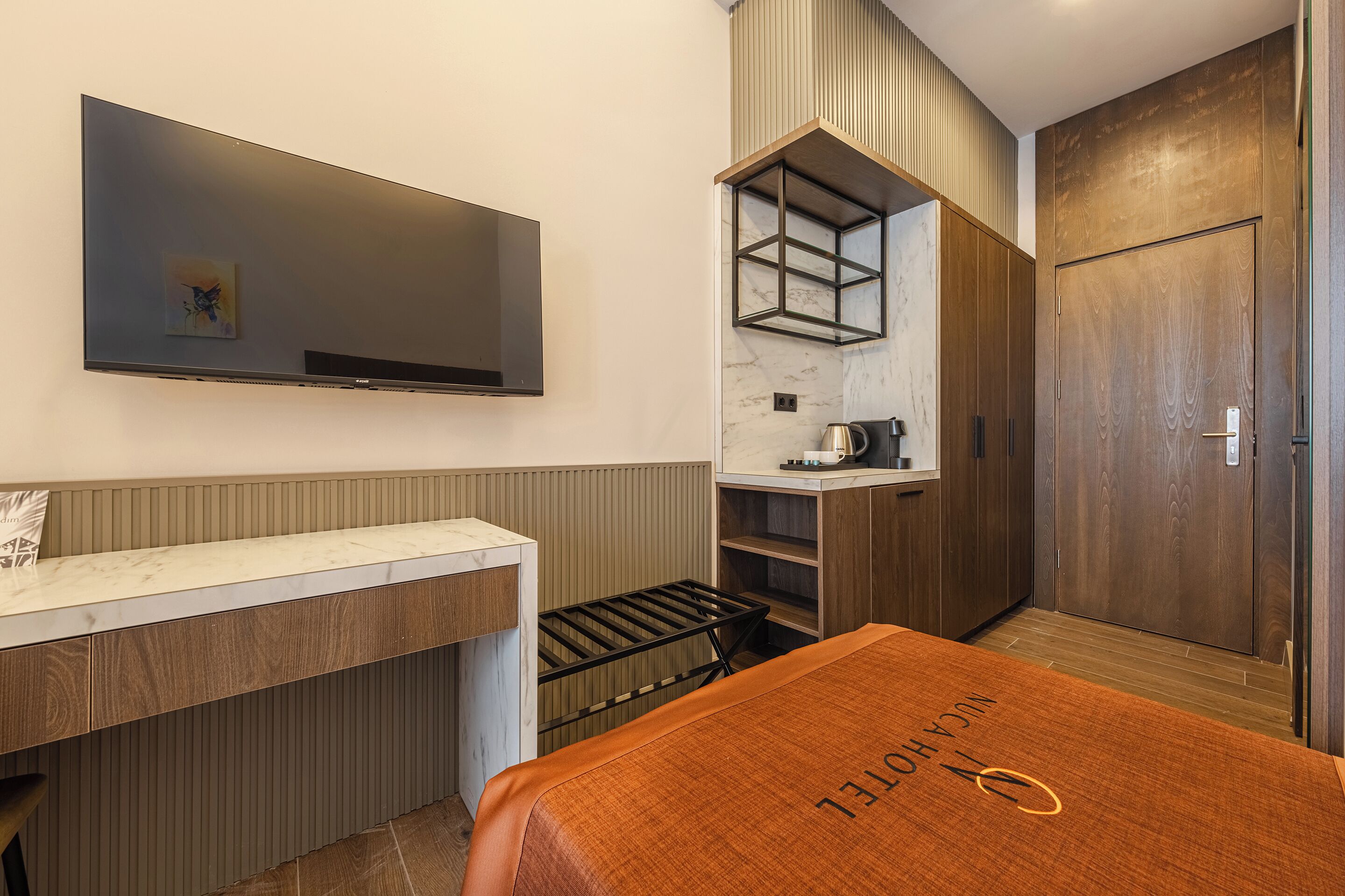 A modern room with a flat-screen TV mounted on the wall, a wooden cabinet with a marble countertop, a built-in shelf, and a door with a wooden finish.