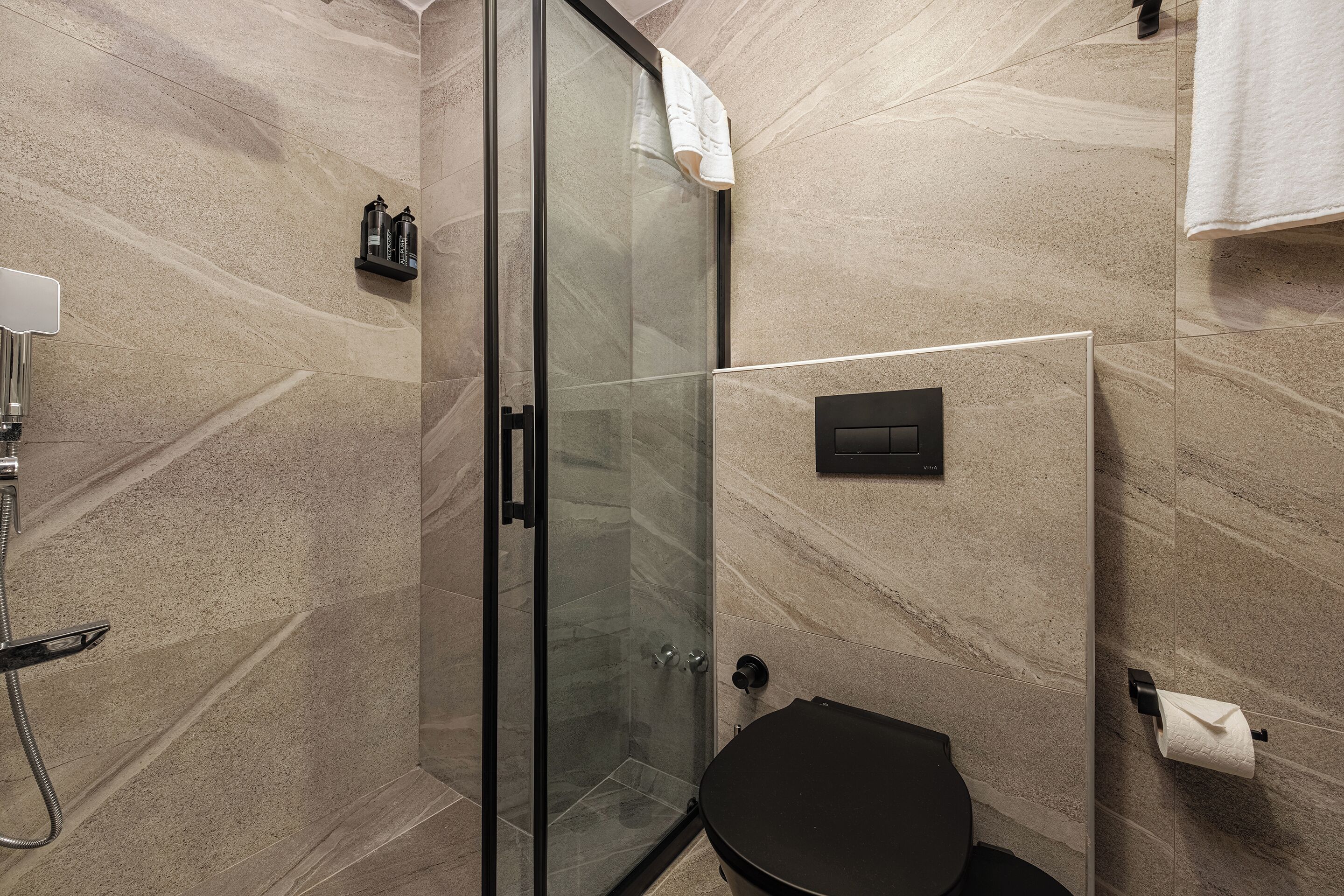 A modern bathroom with a glass-enclosed shower, a black toilet, and a marble-tiled wall.