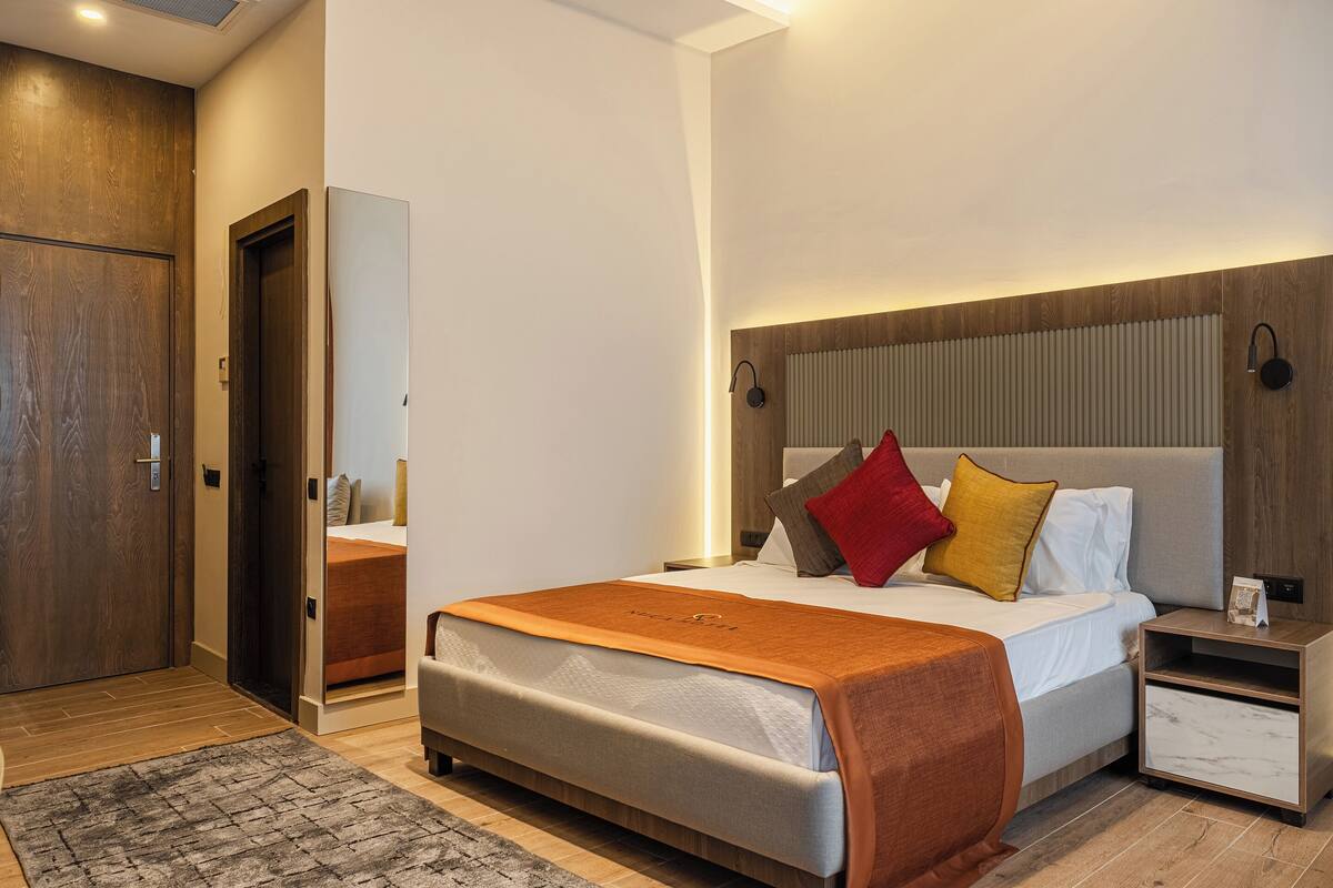 Una habitación de hotel moderna con una cama grande, una mesita de noche y una puerta de madera.