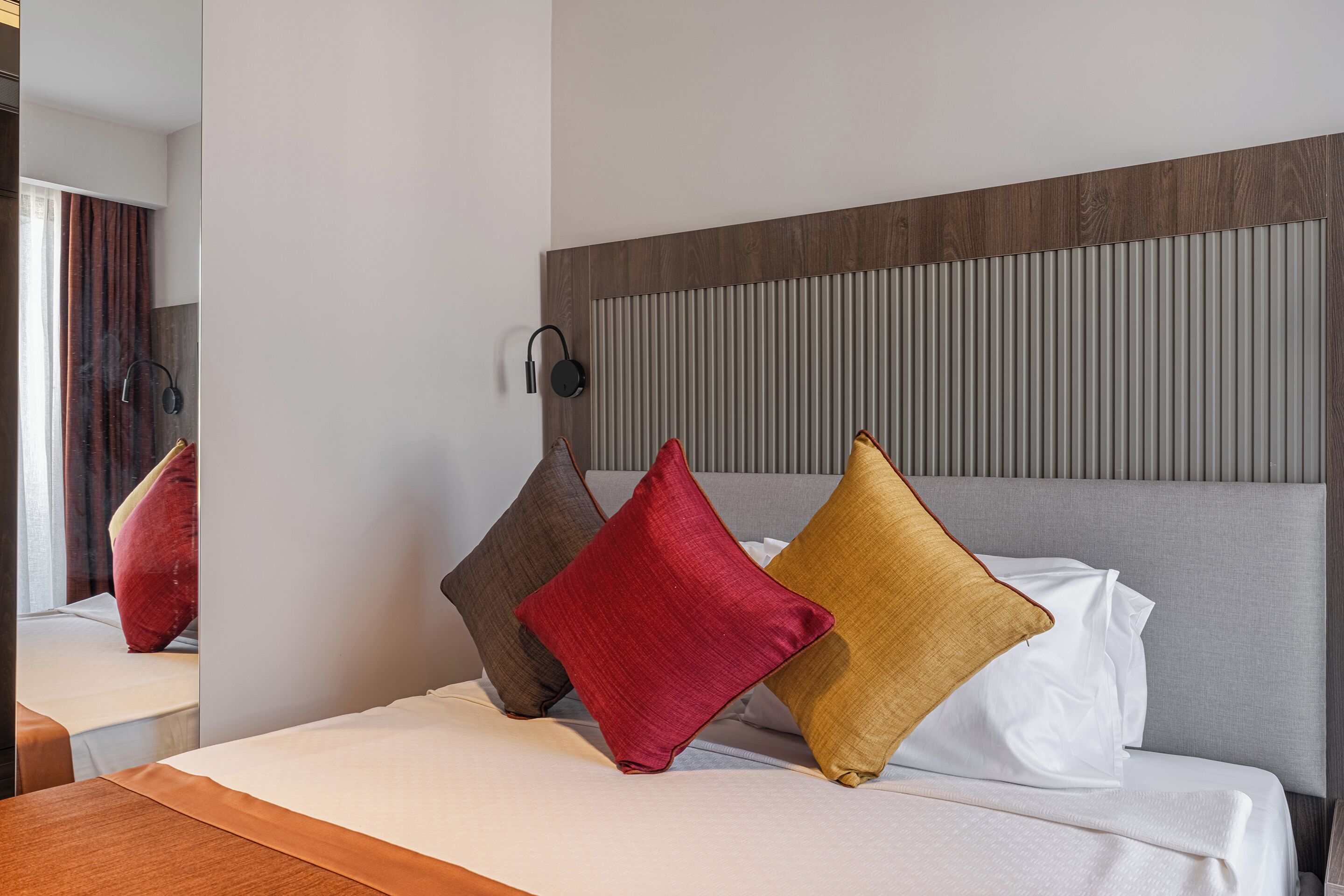 Habitación de hotel con cama, almohadas, cabecero y lámpara fijada a la pared.