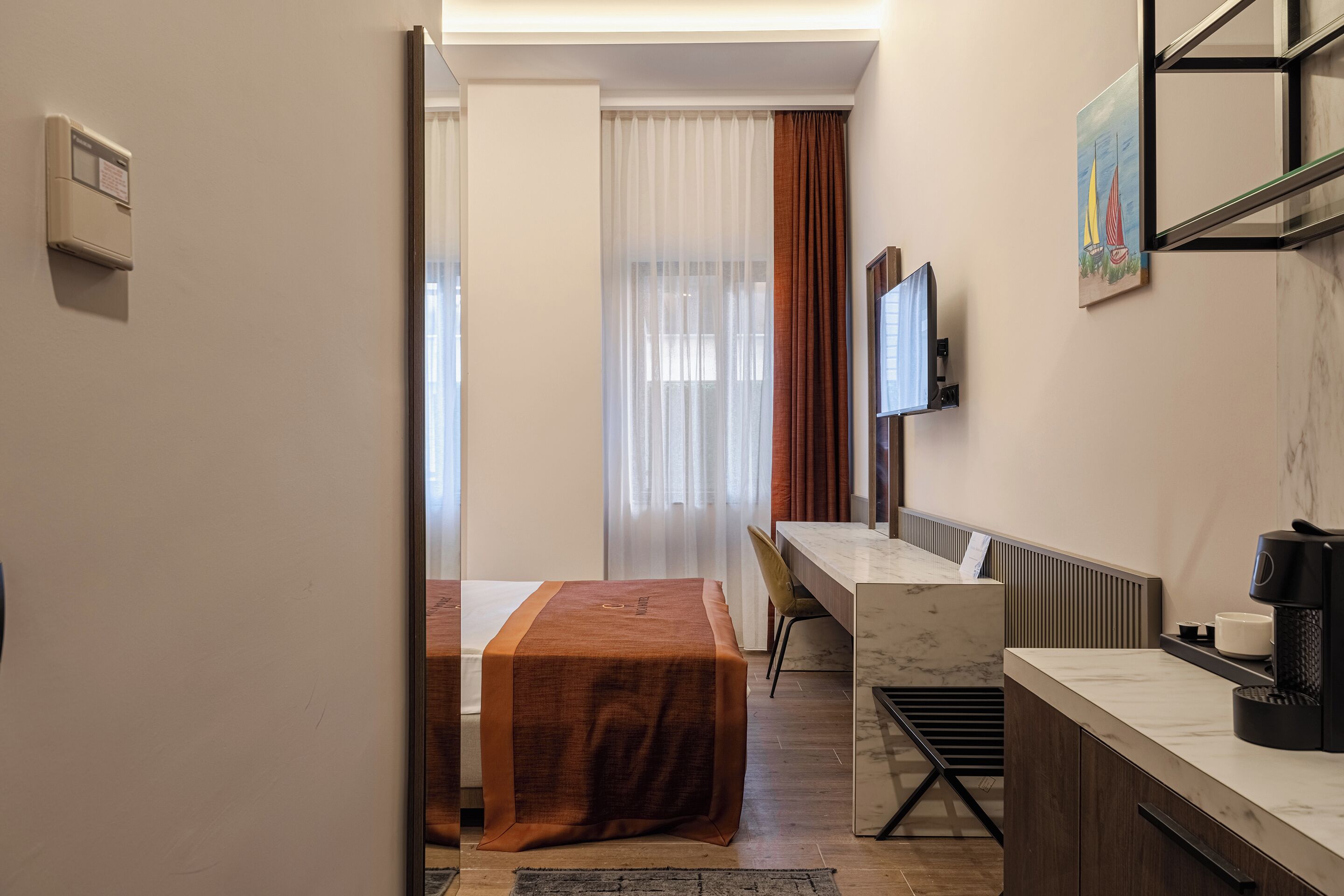 A hotel room with a bed, a desk, a chair, a TV, and a coffee machine.