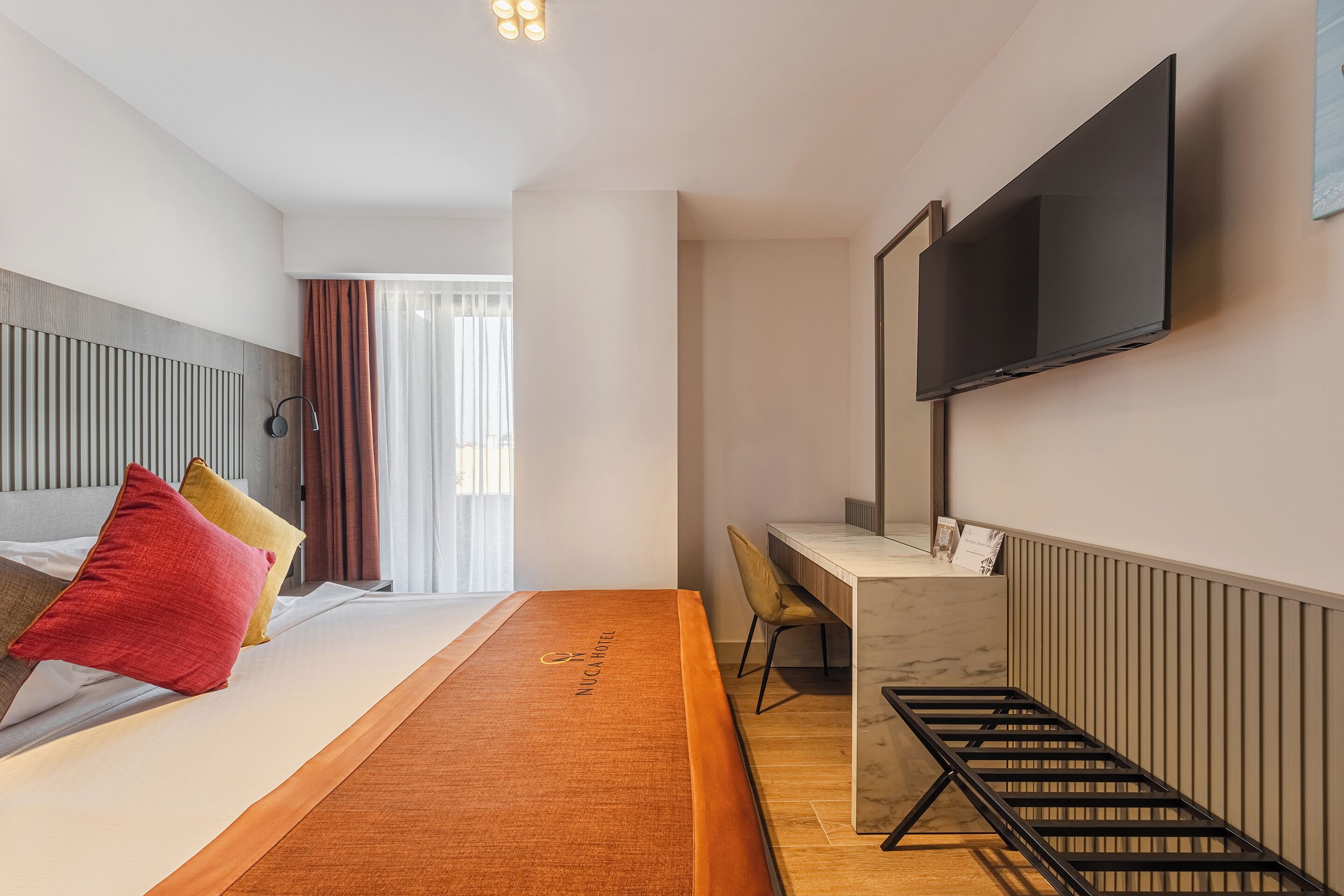 A hotel room with a bed, a desk, a chair, a TV, and a window with curtains.