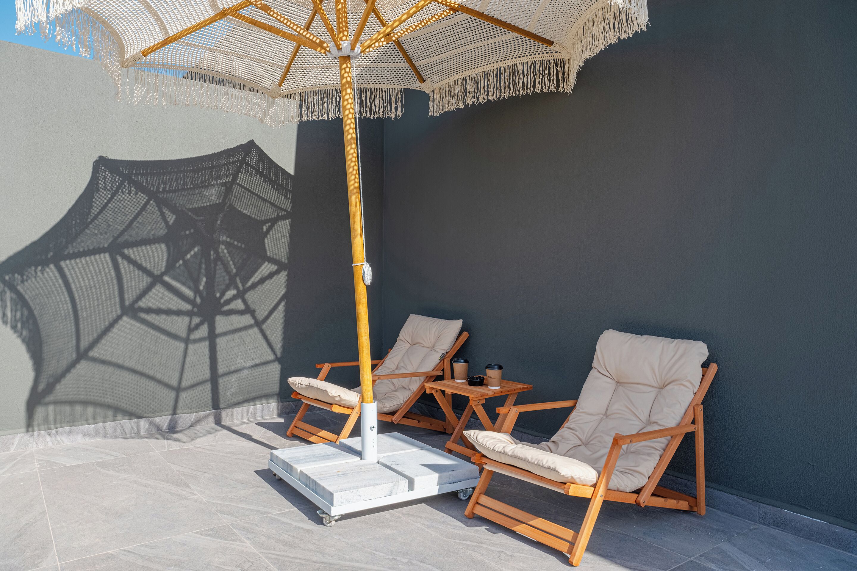 A sunlit outdoor seating area with a large umbrella, cushioned chairs, and a small table with a cup and saucer.