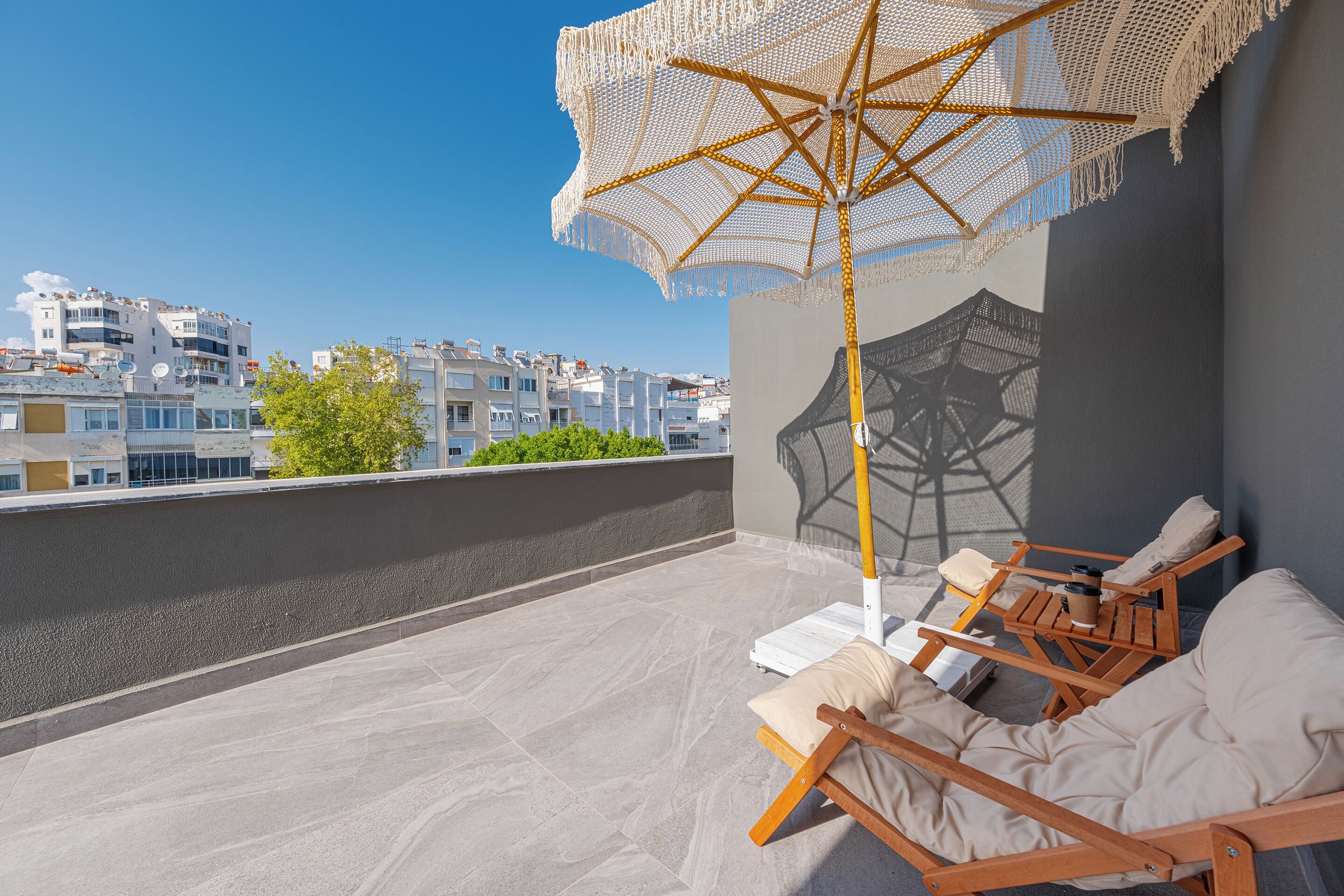 A rooftop terrace with a large umbrella, wooden lounge chairs, and a view of buildings in the background.
