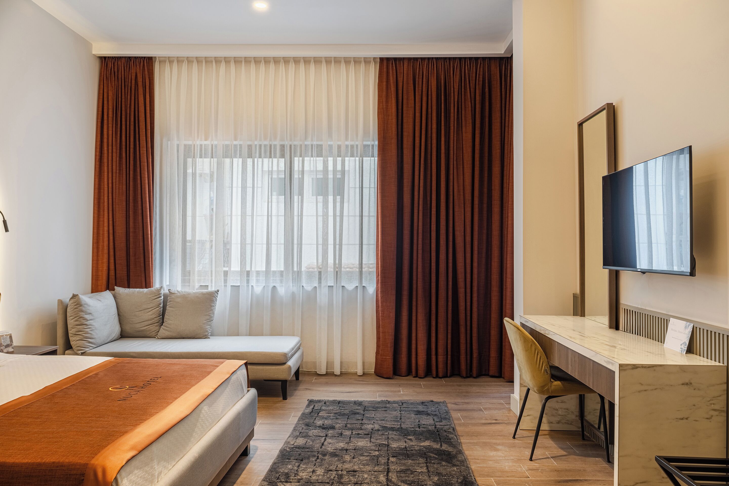 A hotel room with a bed, a desk, a chair, a TV, and a window with curtains.