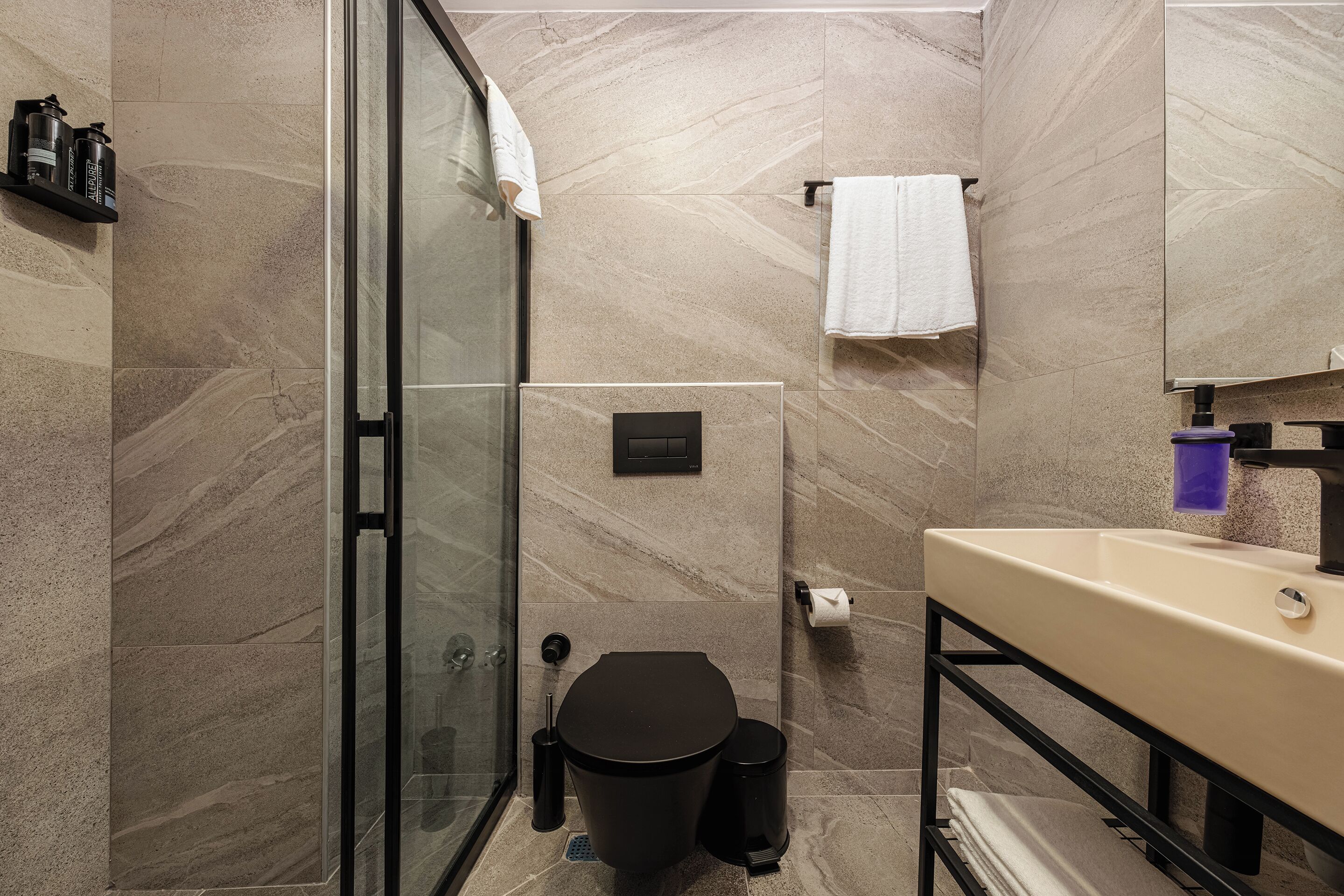 A modern bathroom with a glass shower enclosure, a black toilet, and a beige sink with a mirror above it.