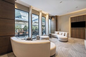 A modern living room with large windows, a flat-screen TV, and a seating area with a sofa and ottoman. - Mira Inn Lara (Antalya)