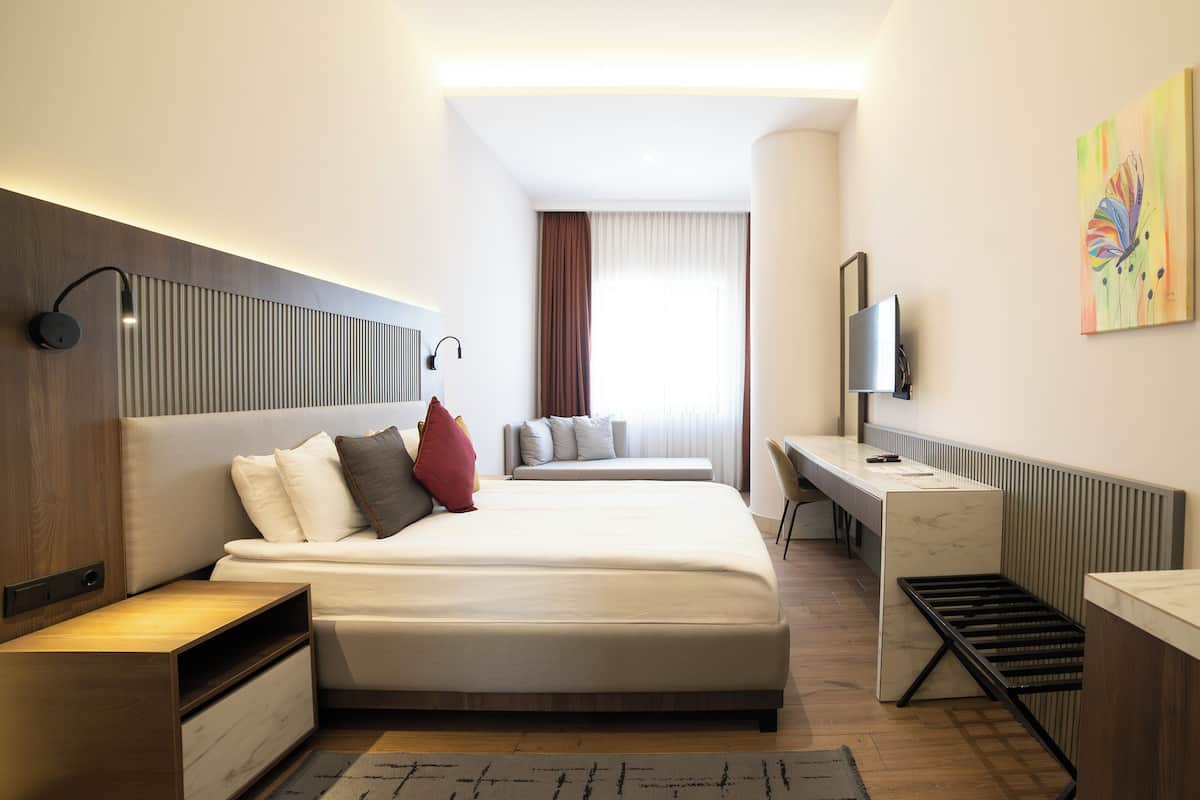 Una habitación de hotel moderna con una cama grande, mesitas de noche, un escritorio y un televisor.