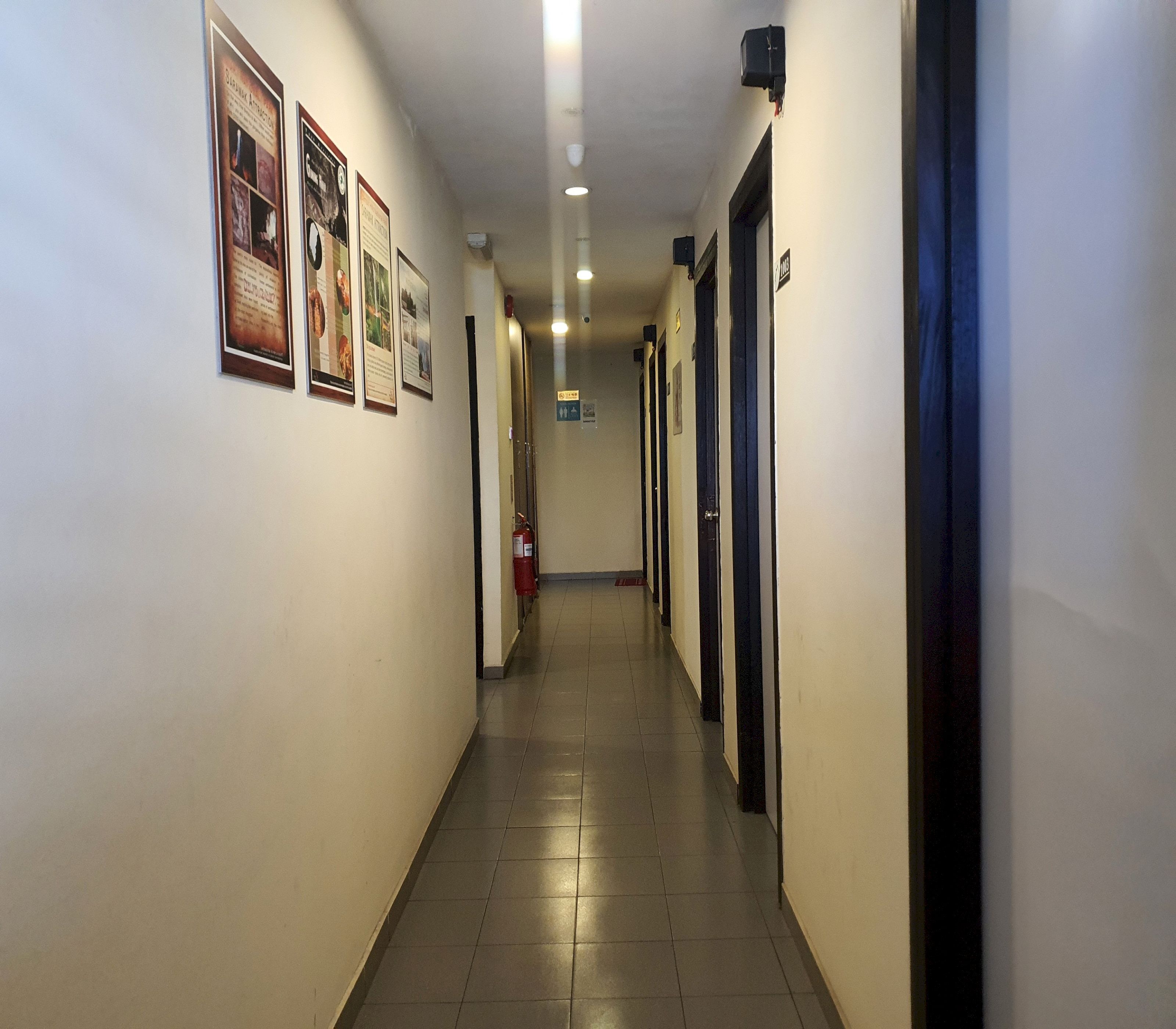 A hotel hallway with framed informational posters on the walls, a fire extinguisher, and doors on the right side.